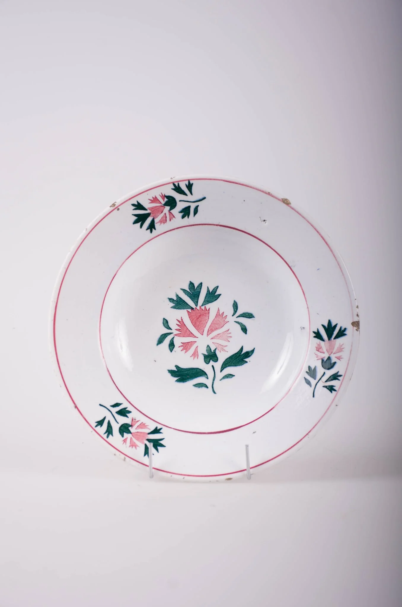Farfurie de formă tronconică, adâncită; pe fund are găuri pentru agățare. În centru și pe margine este decorată cu motive fitomorfe și florale; pe margine sunt trei flori cu frunze încadrate de două cercuri concentrice; în interior este doar o floare cu frunze. Cromatică: fond: alb; motive: vișiniu; verde., detail