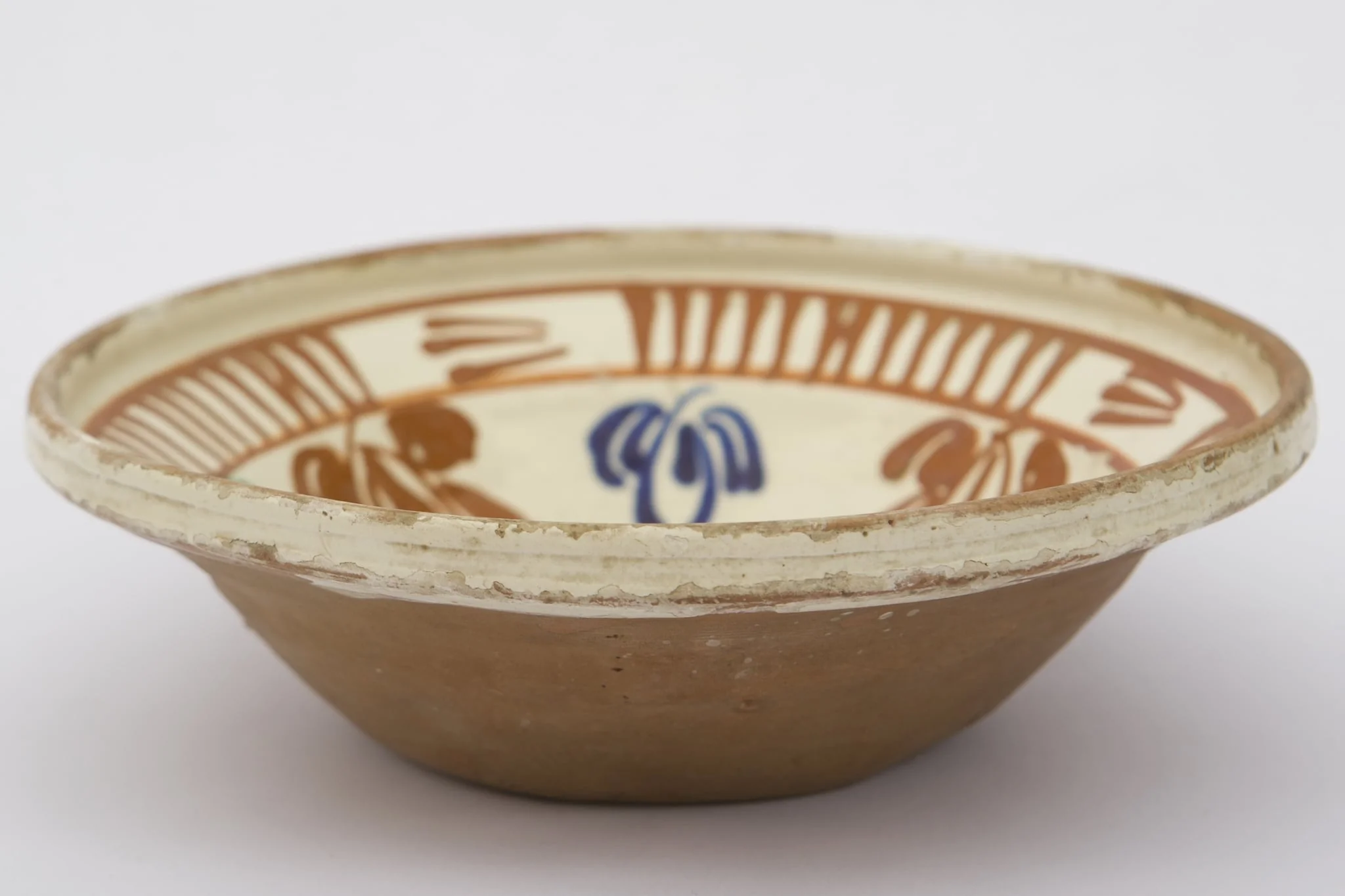 Piesă ceramică de dimensiuni medii, smălțuit la interior, având formă tronconică, cu baza plată, pereții ridicați și buza evazată. Întreaga suprafață interioră a piesei a fost decorată cu motive geometrizante și fitomorfe stilizate. O floare, cu petale verzi, roșii și albastre și cu un punct roșu în mijloc, este mărginită de un brâu circular, compus din opt reprezentări florale, cu aceiași cromatică. Marginal, pe buza piesei a fost realizat cel de-al doilea registru: două linii circulare, care încadrează patru registre, compuse din linii verticale, despărțite de alte patru registre din linii orizontale (2-3 linii). Farfuria era folosită în gospodărie pentru decorarea interioarelor. Prezintă uzură funcțională. Cromatică: fond: cărămiziu (exterior); crem (interior); motive: roșu; albastru; verde., detail