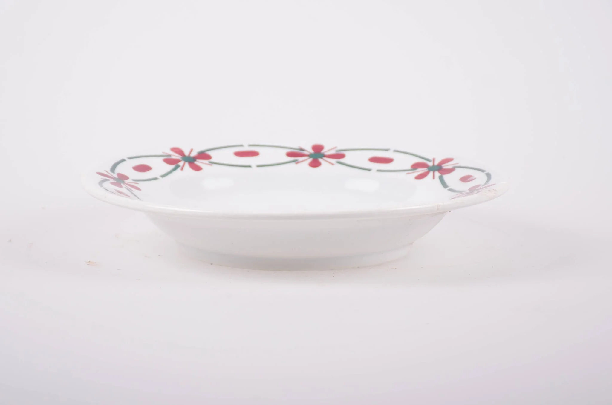 Farfurie din porțelan de formă tronconică. Pe fond alb, marginea este decorată cu flori stilizate. Cromatică: roșu și verde; interiorul farfuriei prezintă flori în: roșu; albastru; verde., detail
