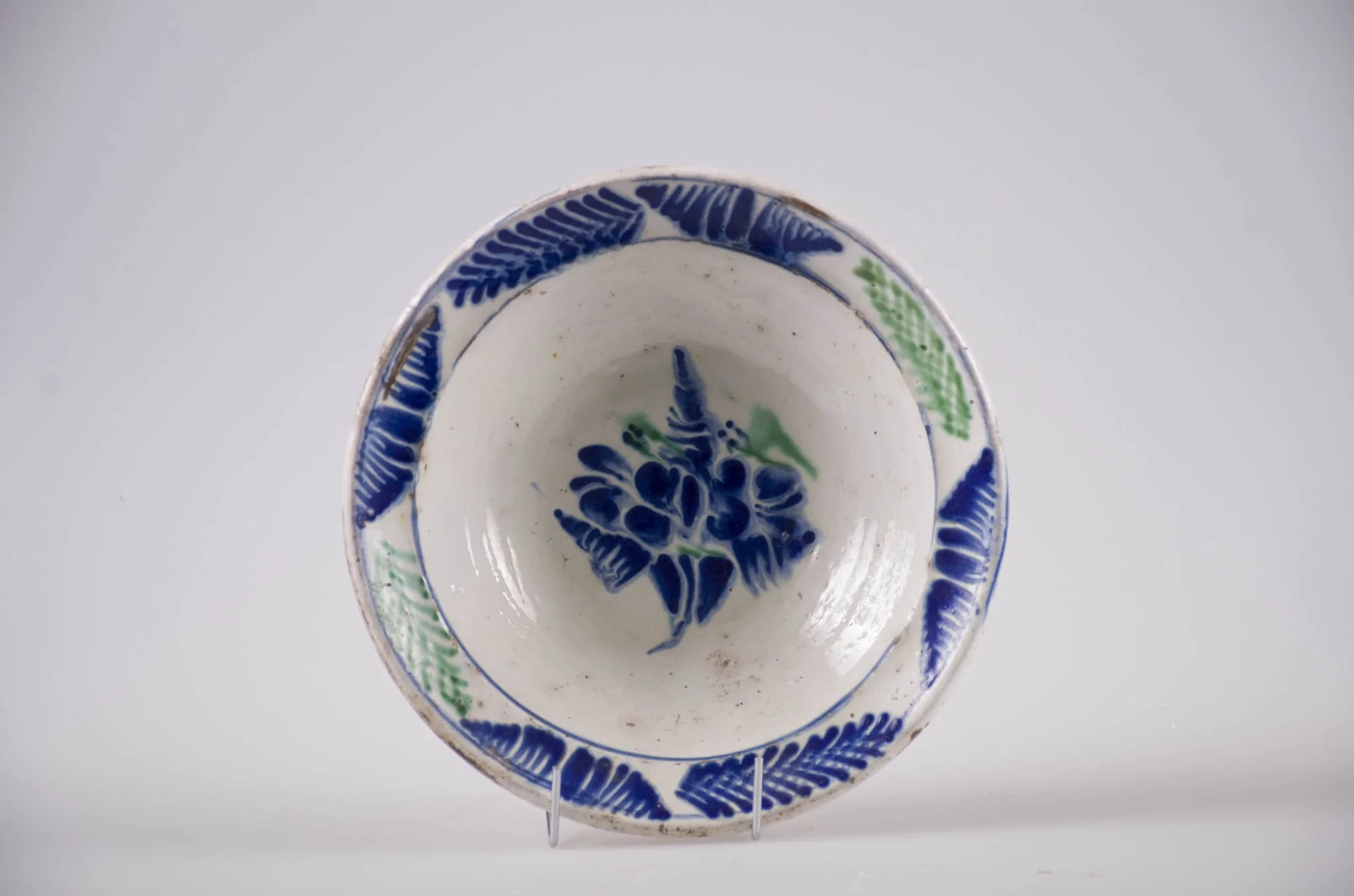 Blid de formă tronconică cu buza evazată, Smălțuit la interior. Decorul este format din ornamente florale dispuse pe motiv central: floare; motive marginale, fitomorfe: brăduț. Cromatică: verde și albastru pe fond alb., detail