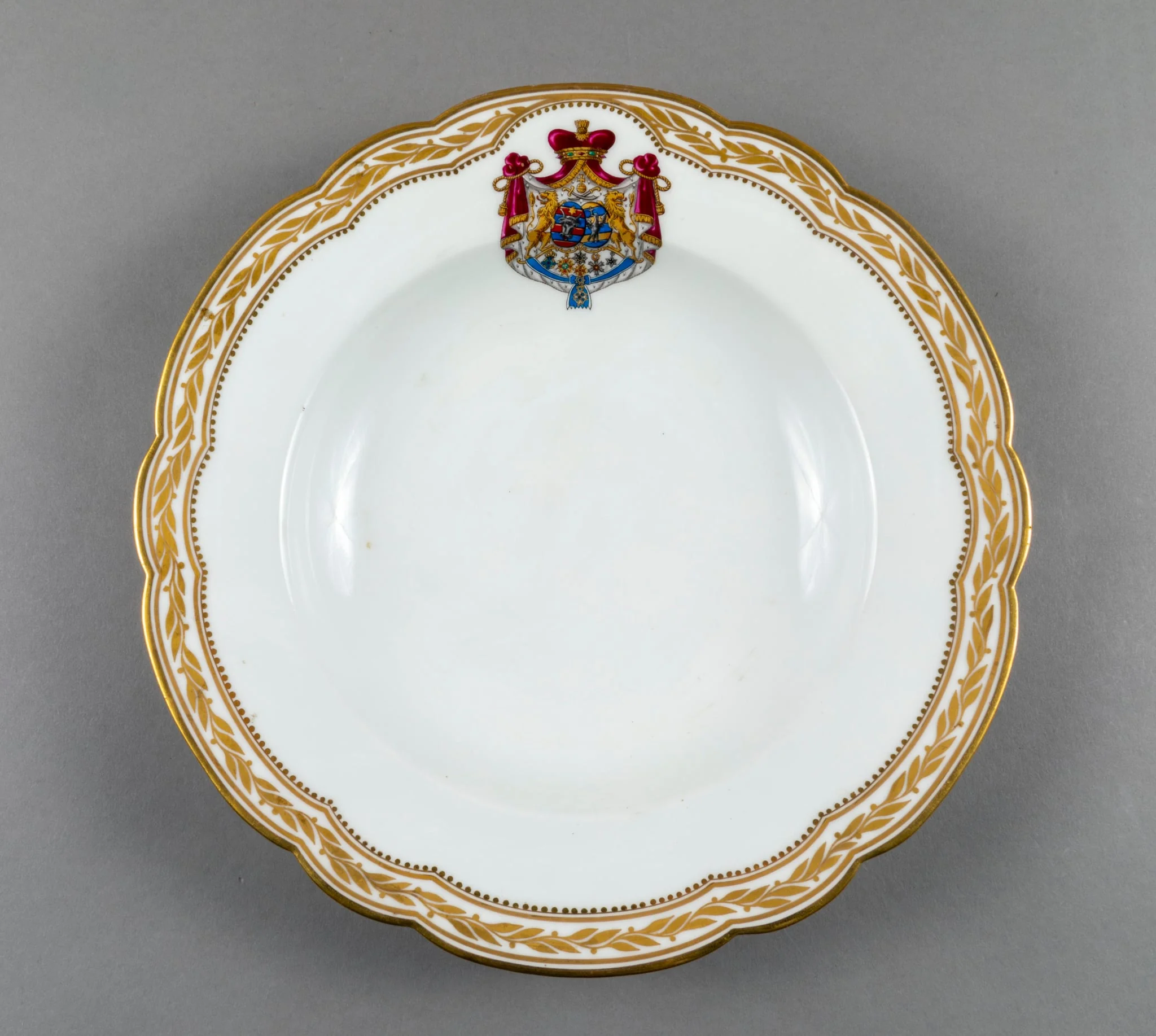 Farfurie adâncă de porțelan de Sevres, realizată din porțelan alb, cu margini treflate, decorate cu frunze de laur pictate, în centrul decorațiilor având blazonul familiei Suțu. Blazonul a fost adesea confundat cu cel al Principatelor Unite, fiind format din: stemele celor două țări românești: prima cea a Moldovei, cea de-a doua cea a Țării Românești, steme plasate pe două scuturi ovale, în fascie, acolate, puțin suprapuse, cea a Moldovei având capul de bour de argint cu stea în șase colțuri de aur, pe un scut cu segmente verticale egale roșii și albastre; cea a Țării Românești având acvila cruciată de argint, cu crucea de aur, scutul având segmente verticale galbene și albastre. Cele două scuturi au ca tenanți doi lei aurii, deasupra armele familiei Suțu – iataganul și sabia, ambele aurii, precum, pe un pavilion de purpură căptușit cu hermină, brodat cu ciucuri de aur și prins într-o coroană cu pietre scumpe. Pe scut, în partea inferioară se află și decorațiile familiei Suțu. Familia Suțu a fost o familie fanariotă grecească, venită în principate în cea de-a doua parte a secolului al XVIII-lea, având trei domni în ambele țări Românești (Alexandru Suțu, Mihai Suțu și Grigore Suțu). Blazonul familiei poate fi admirat inclusiv pe clădirea Palatului Suțu, astăzi Muzeul de Istorie a Municipiului București. Farfuria are marca atelierului Sevres și modelul din anul 1844, precum și seria., detail