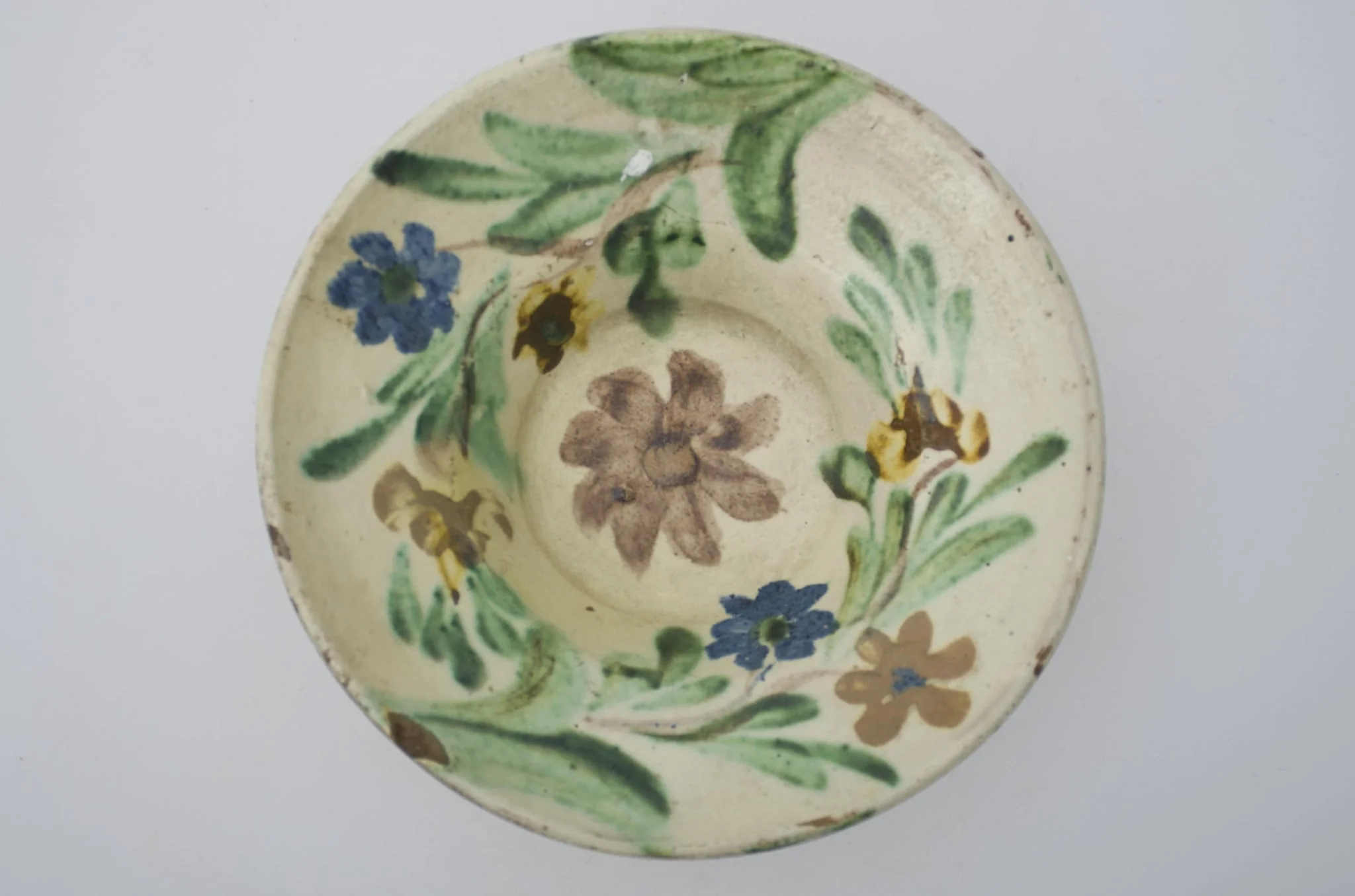 Farfurie cu marginea foarte lată și evazată, smălțuită în interior. Decor floral pe toată suprafața interioară. Cromatică: fond: alb; motive: brun; verde; galben; albastru., detail
