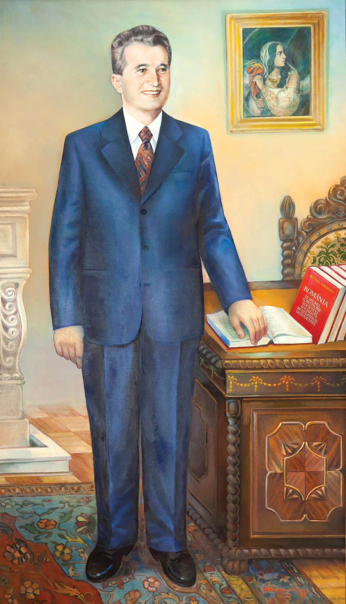 Tablou ulei pe pânză, portret Nicolae Ceaușescu, semnat în partea dreaptă jos Romulus Constantinescu, datat 1983. Nicolae Ceaușescu este reprezentat într-un costum albastru metalizat, stând în picioare lângă biroul său cu mâna pe unul din volumele lucrării ”România pe calea construirii societății socialiste multilateral dezvoltate”. Pe peretele din spatele său ”România Revoluționară” a lui C.D.Rosenthal. Comandat și oferit de Comitetul Județean de Partid Argeș (1983)., detail