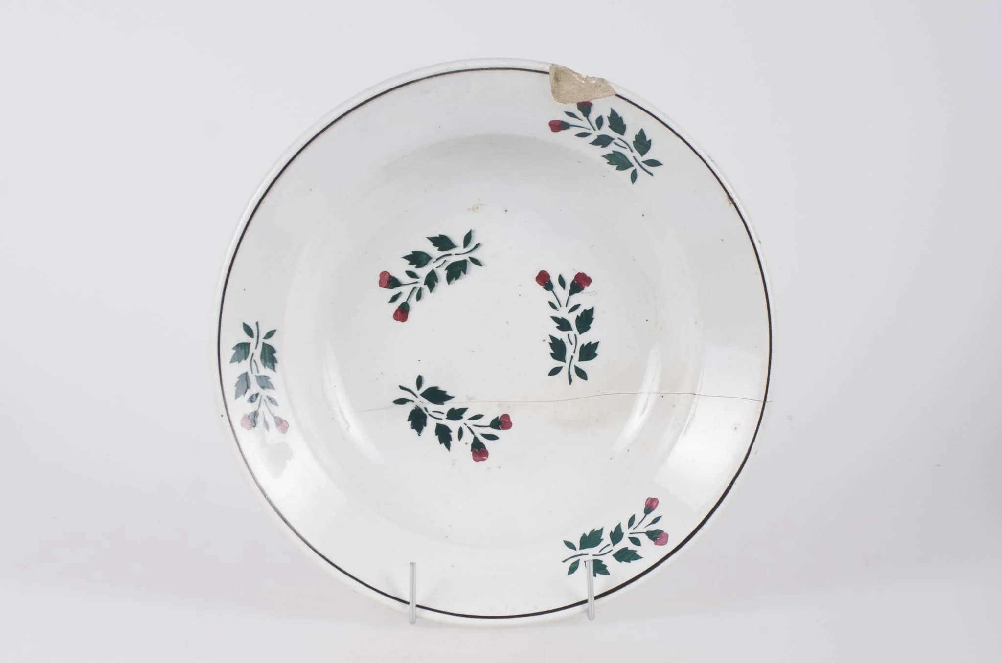 Farfurie din faianță smălțuită cu smalț alb. Vasul este de formă circulară, ușor adâncită. Pe fundul vasului decorul este floral-vegetal. Pe buza vasului se identifică trei flori, un decor geometric (cerc) ce încadrează decorul floral. Pe fundul vasului se identifică marca ”WILHELMSBURG”. Cromatică: fond alb; motive: verde; roșu., detail