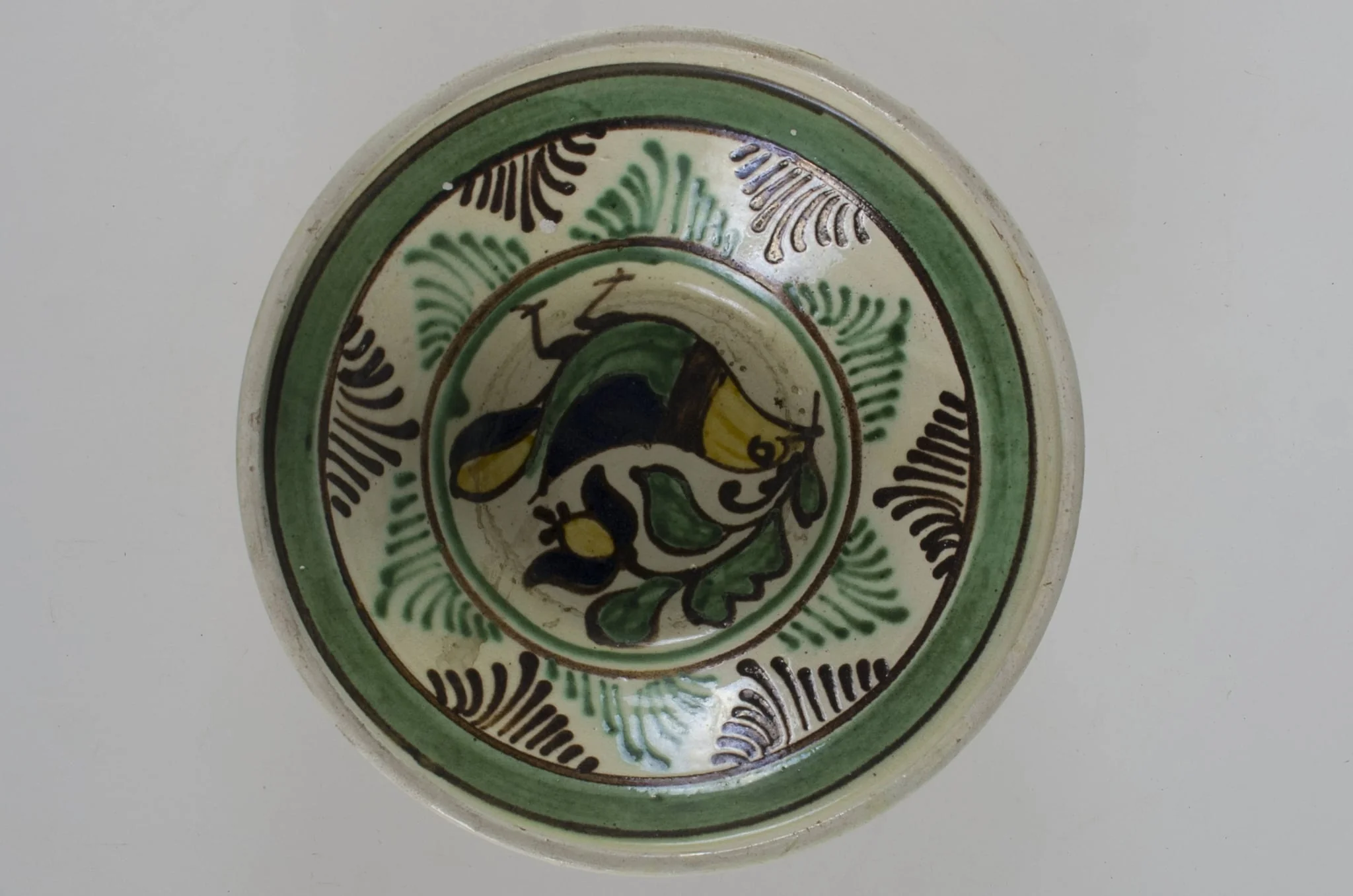 Blid de formă tronconică, adâncit, cu buza înălțată și ușor evazată. Este smălțuit în interior și în exterior (buza). Decorat la interior cu motive avimorfe și fitomorfe, încadrate de două cercuri concentrice; pe margine, în interior este decorată cu linii și brăduț stilizat, iar în exterior cu două linii; pe fund are două găuri pentru agățare. Cromatică: fond: gri (exterior); alb (interior); motive: maro; verde; galben; negru., detail