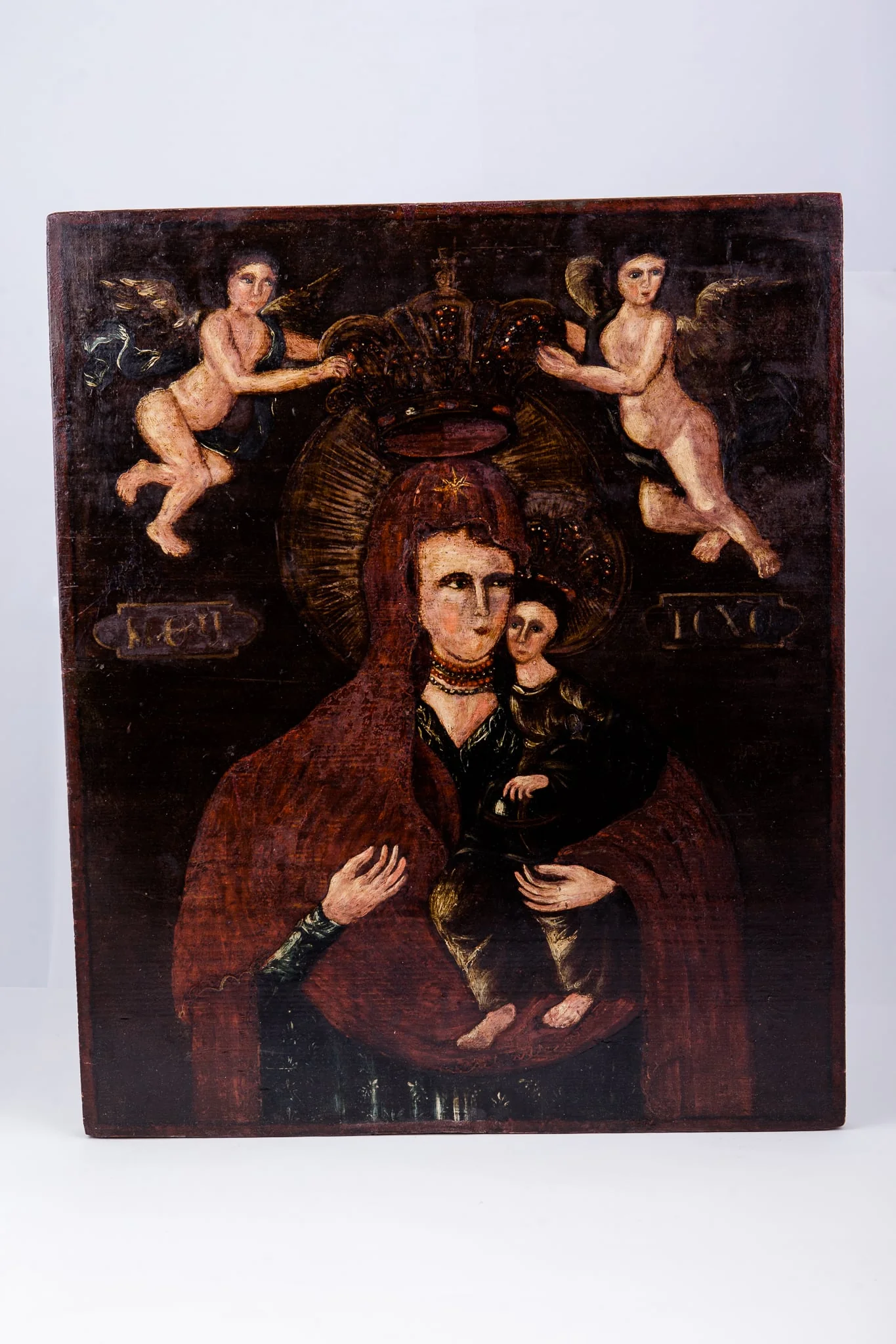 Maica Domnului ține în brațe Pruncul Iisus Hristos, care arată cu mâna dreaptă înspre Maica Domnului, prezentându-ne-o. Maica Domnului este înveșmântată în mantie cu maforion roșu-stacojiu, cu interiorul negru. Maica Domnului are aureola în raze luminoase de soare. Pruncul Iisus Hristos este înveșmântat cu sacos și omofor brun spre negru, cu coroană și aureolă pe cap. Fondul icoanei este negru întunecat, în contrast fiind cu lumina chipurilor și cromatica veșmintelor. În registrul superior sunt doi îngeri îndreptați spre coroana stilizată a Maicii Domnului, făcând gestul Încoronării. Îngerii sunt pictați asemenea unor putti, din pictura barocă. Cromatică este armonioasă: roșu stacojiu, brun, acajou, brun-ocru, brun, bej, alb, verde-olive, negru. Inscripția din româno-chirilică se traduce MP IC XC Maica Domnului Iisus Hristos. Icoana este pictată în manieră barocă și are atmosfera catolică., detail