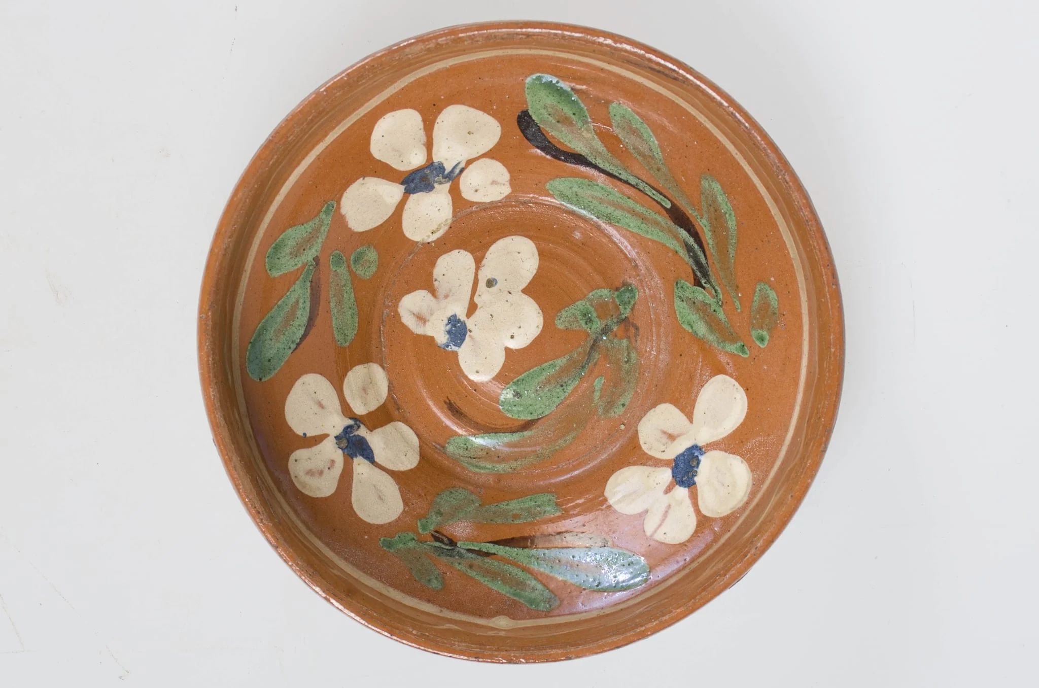 Blidul de formă tronconică adânc, smălțuit (la interior). Acesta este ornamentat cu motive florale, având cu buza înaltă. Blidul este neornamentat la exterior, fiind smălțuit (la exterior) doar pe buză. Pe exteriorul buzei este incizată o linie. Fundul obiectului are formă circulară, fiind prevăzut cu două orificii pentru prindere. Cromatică: fond: cărămiziu (exterior); alb (interior); decor: verde; alb; albastru; maro., detail