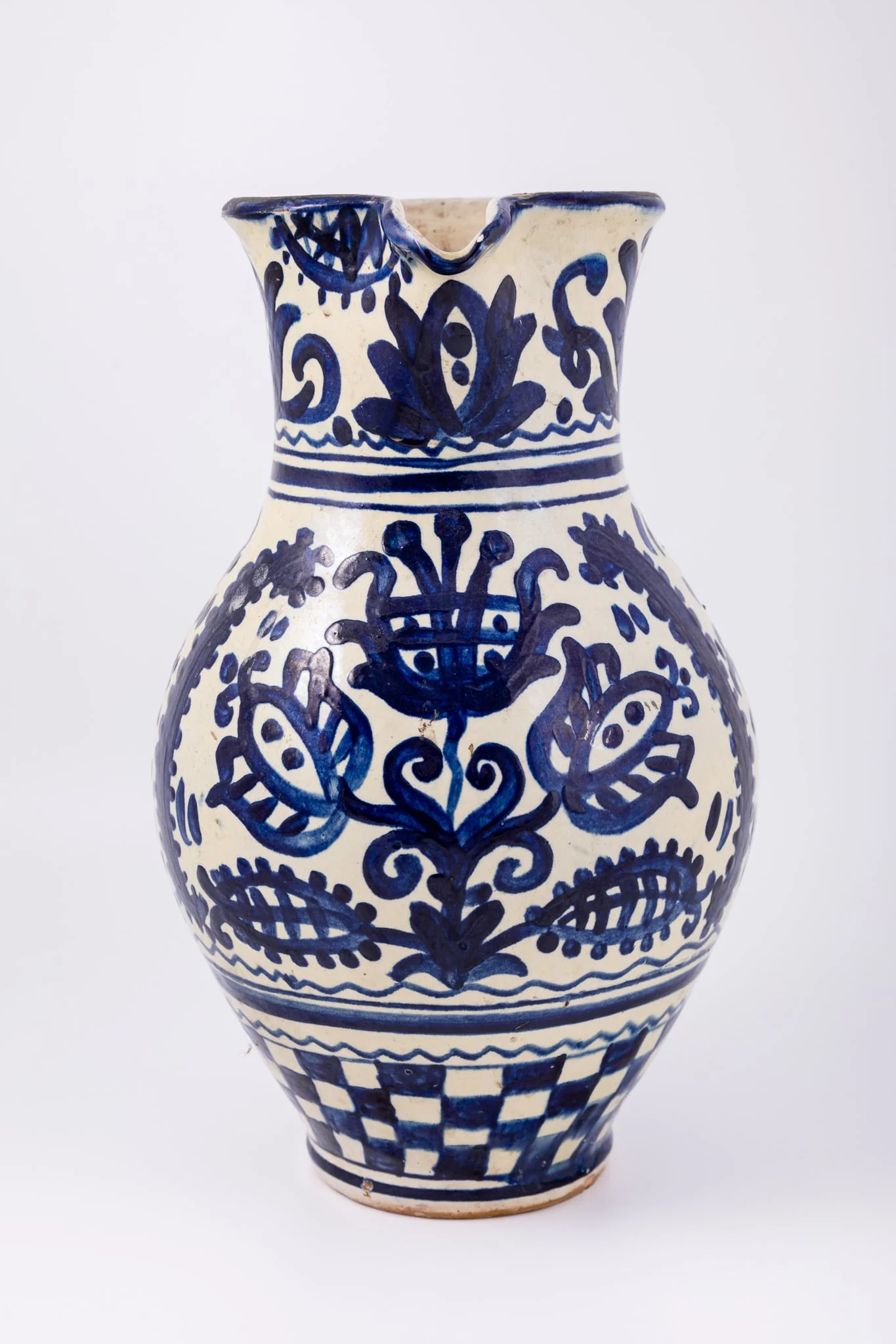 Cană piriformă prevăzută cu o toartă dreaptă și lată, gura rotundă, prevăzută cu cioc de scurgere. Suprafața decorativă a vasului este împărțită în patru registre decorative. Primul registru dispus pe gâtul piesei prezintă un decor floral și fitomorf reprezentând lalele și lujeri. Al doilea registru prezintă o linie vălurită și trei linii subțiri circulare. Decorul central, reprezintă trei „arbori ai vieții” stilizați realizați din trei lalele mari, înflorite, lujeri și frunze, separați de câte o semilună. Registrul al patrulea prezintă motivul tablei de șah. Deasupra toarte pictate cu motive florale și fitomorfe este redat anul confecționării piesei: 1980, iar pe fundul vasului numele persoanei care a pictat piesa: Herta Wilk. Cromatica: alb, albastru-cobalt., detail