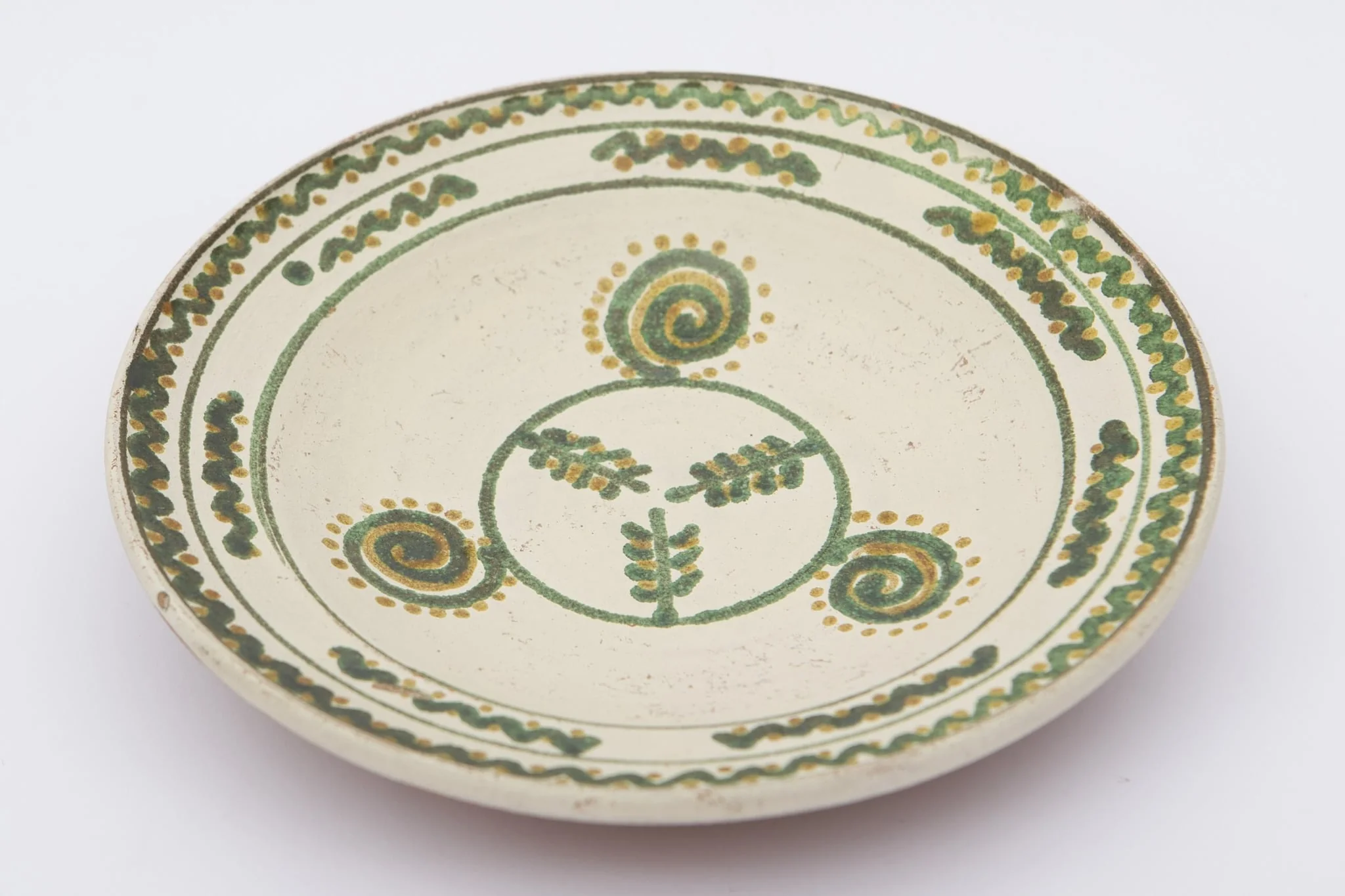 Vas ceramic de formă rotundă și profil tronconic aplatizat cu pereții larg evazați. Fața farfuriei a fost introdusă în angobă albă, decorația a fost făcută cu pensula. Pe fundul vasului sunt trei crengi de brad circumscrise. Pe pereți au fost pictate trei spirale punctate. Buza a fost împărțită în două registre: primul cu șapte valuri întrerupte; al doilea val continu, punctat. La posterior, baza este perforată pentru atârnare și incizată inscripția ,,D. Șchiopu''. Cromatica: fond: motive: verde, galben., detail