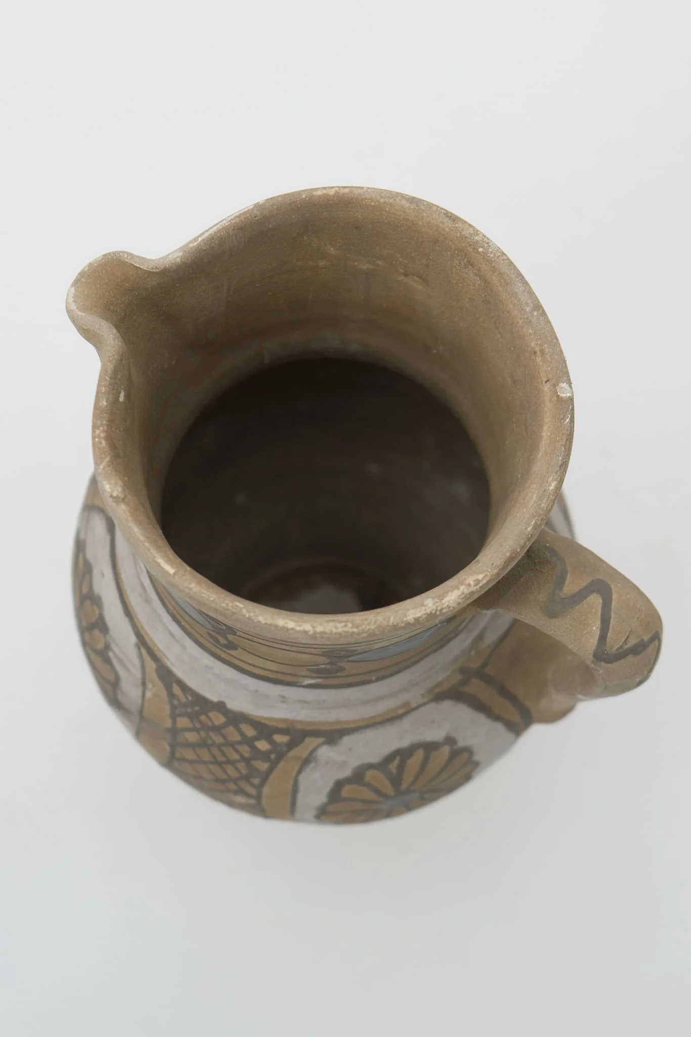 Cană de vin de formă bitronconică cu gâtul lung și buză dreaptă cu cioc. Registrele ornamentale se succed de jos în sus, delimitate de cercuri concentrice, și prezintă pe corpul vasului motive florale și geometrice sub formă de hașură întrerupte de partea de sus de o zonă cerc alb mai gros și mai apoi continuat cu cercuri concentrice ce delimitează de mijloc și de sub buză două cercuri albe groase (angoba). Cromatică: fond: alb; cărămiziu; motive: maro; gri; albastru., detail