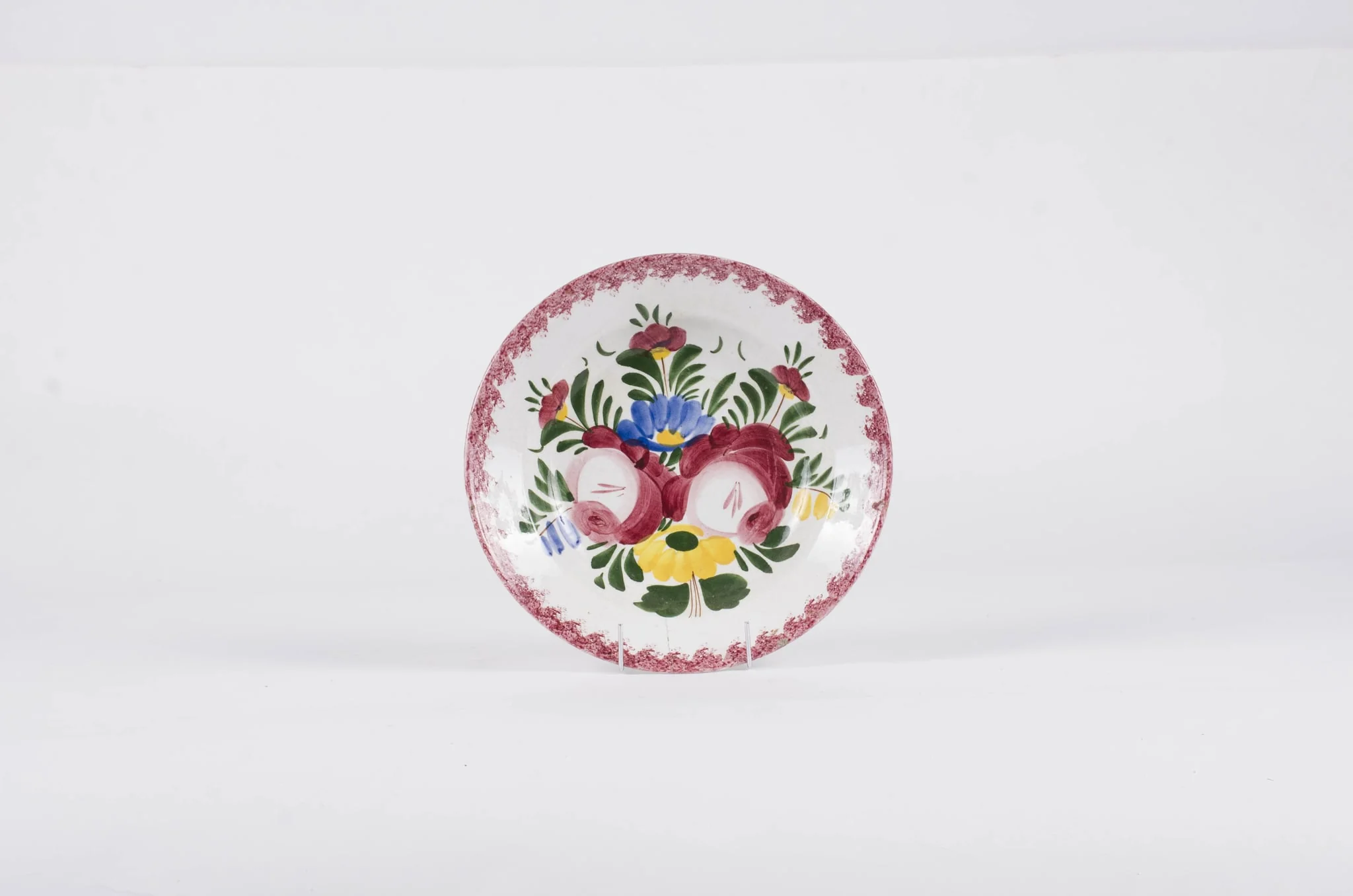 Vasul este de formă tronconică fiind smălțuit interior-exterior. Este confecționat din faianță Decorul este format din motive florale pictate pe fond alb; gura este decorată în stropi de culoare vișinie iar baza farfuriei este decorată cu motive florale. Se identifică șapte flori alcătuind motivul decorativ pe baza farfuriei. Pe spate inscripția este indescifrabilă. Cromatică: galben; albastru; verde; vișiniu; alb;, detail