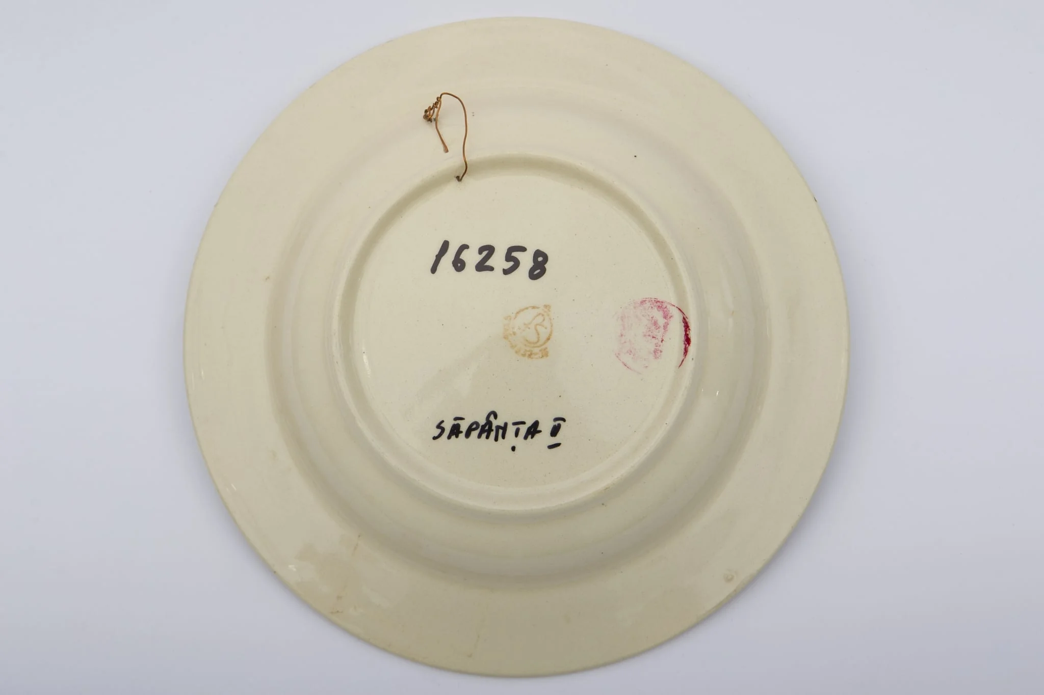 Piesă ceramică smălțuită, de formă circulară, cu baza plată, pereții puțin înălțați și marginile larg evazate. Peste stratul alb de angobă a fost pictat decorul fitomorf stilizat. Central, pe fundul piesei au fost realizați trei trandafiri roșii, însoțiți de patru boboci roșii și frunze verzi. Primul registru este încadrat de cel de-al doilea registru, dispus pe marginea recipientului ceramic. O bandă circulară galbeană peste care au fost realizați șase boboci roșii și frunze maro și verzi, este mărginită de două linii concentrice drepte. Farfuria era folosită în gospodărie pentru servirea hranei sau amenajarea interioarelor. Prezintă uzură funcțională. Cromatică: fond: alb; motive: roșu; verde; galben; maro., detail