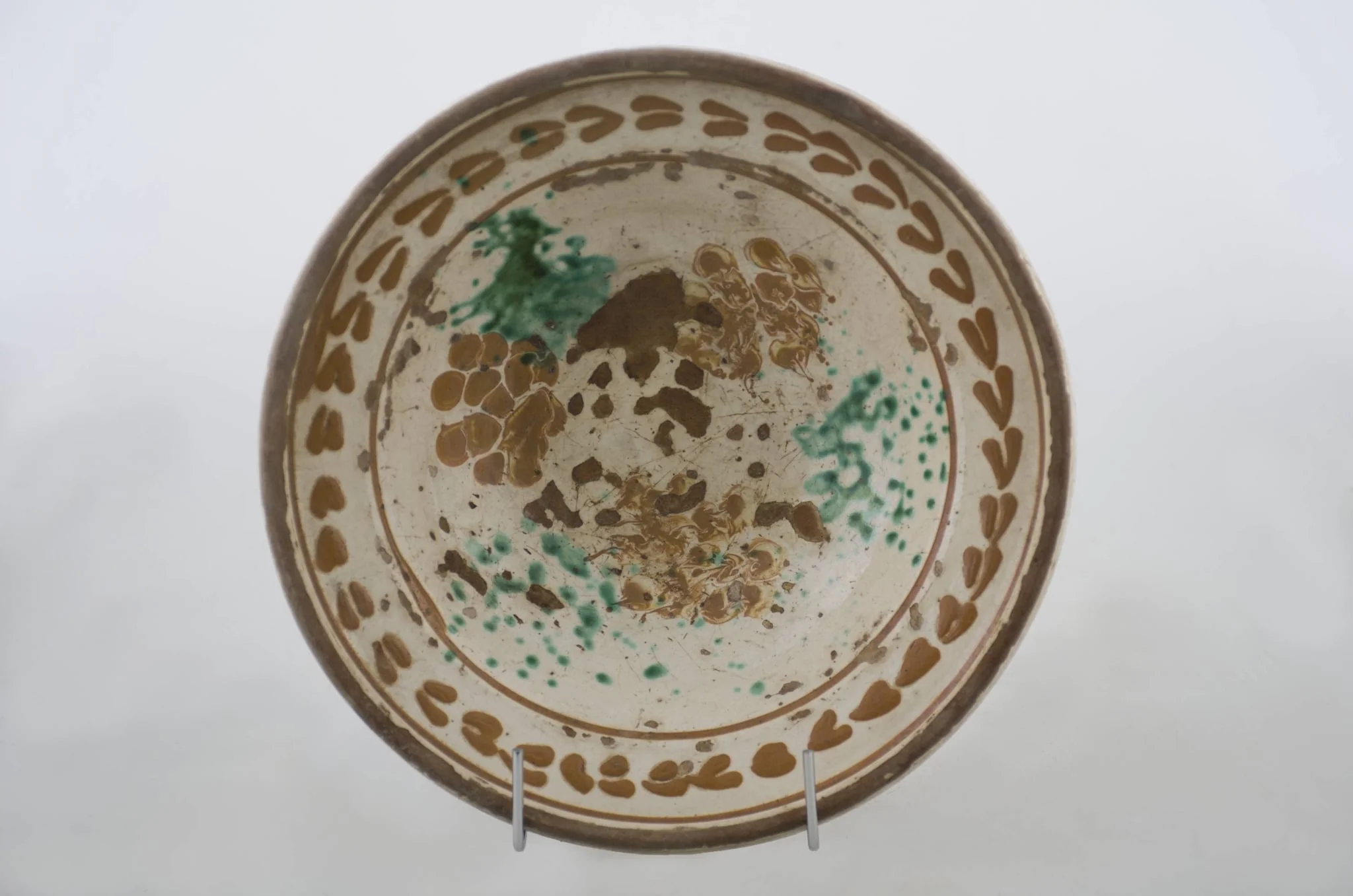 Vas ceramic de formă tronconică cu baza plată, pereții larg evazați și buza dreaptă și înălțată. După modelarea la roată, uscarea și arderea recipientului, a fost aplicat un strat de angobă în interiorul vasului, peste care a fost pictat decorul floral și vegetal stilizat, format din două registre. Primul registru, situat pe fundul și pereții vasului, și încadrat de o linie circulară, a fost decorat cu câte trei pete mari de culoare verde și galben-muștar, realizate prin stropire cu pensula. Al doilea registru, cel care decorează buza recipientului ceramic și este mărginit, la rândul lui de o linie circulară, prezintă elemente ornamentale de tipul „bobului de grâu”. Cromatică: fond: alb; motive: roșu; albastru; verde., detail