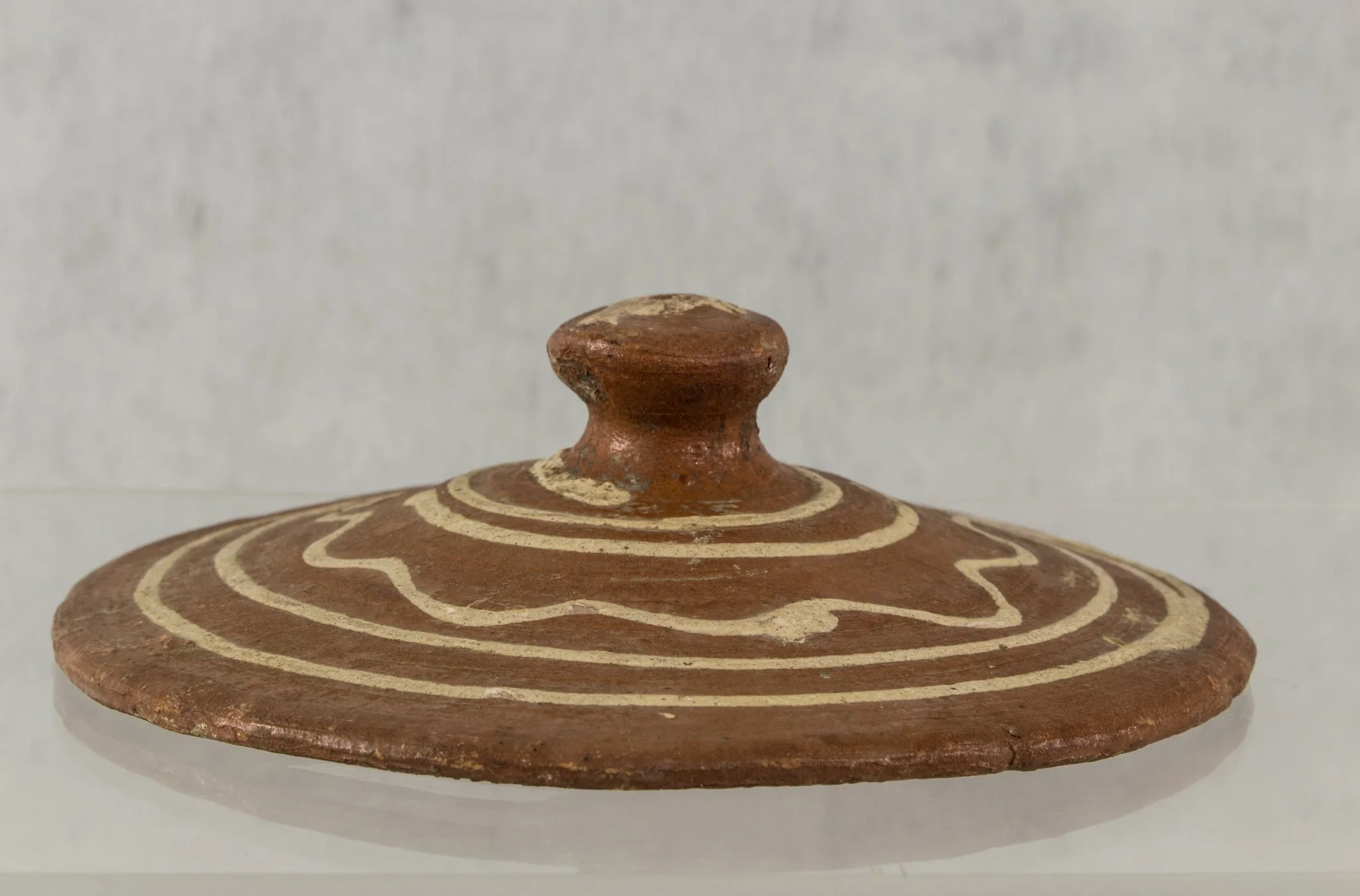 Capac cu buton, în formă de ciupercă, smălțuit pe partea exterioară. Netezire destul de bună la exterior, neglijentă la interior. Decor în trei registre, realizat prin pictare: spirală deschisă, cerc vălurit, spirală închisă. Cromatică: alb, cărămiziu., detail