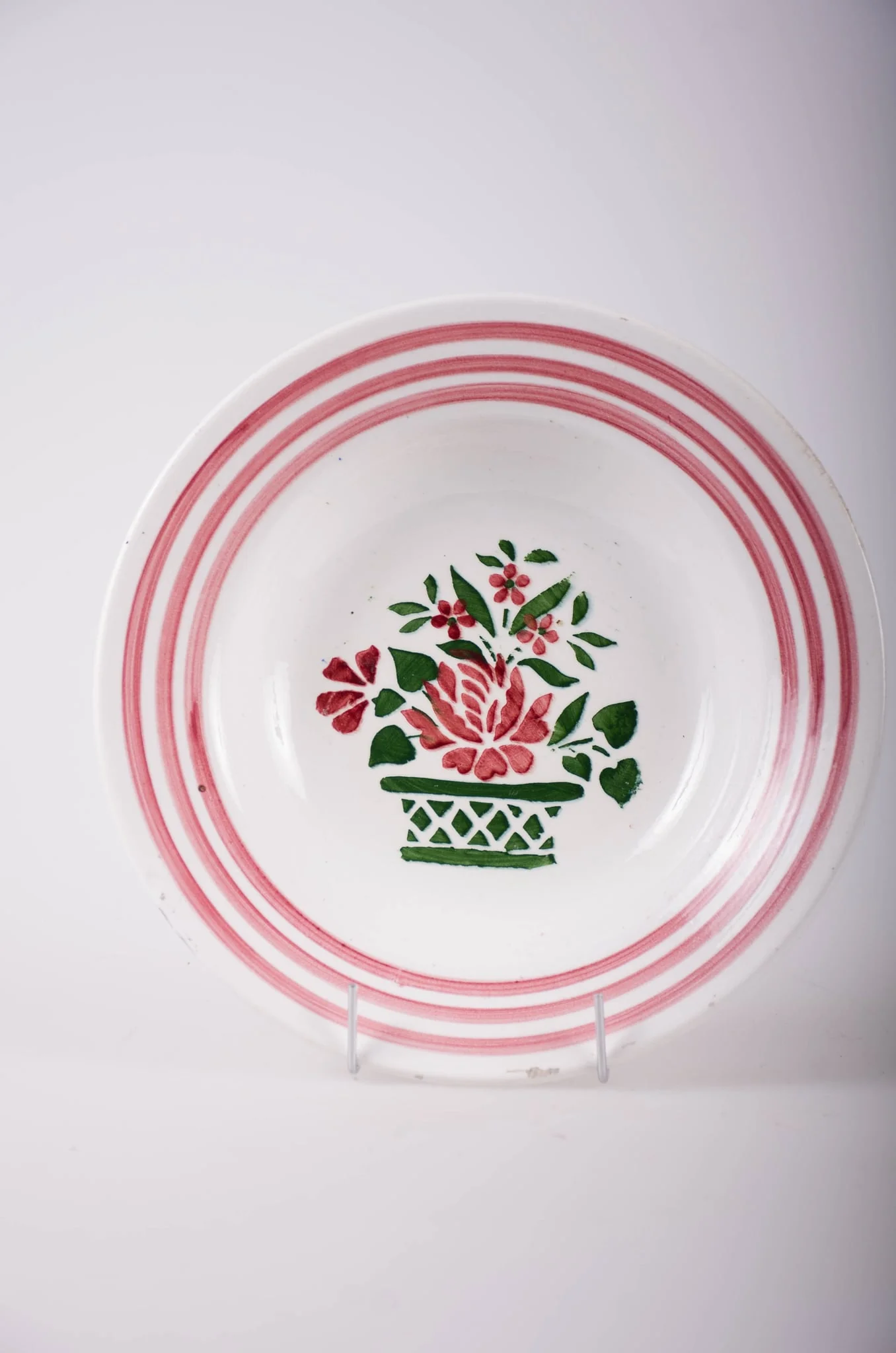 Vas de formă tronconică, adâncit; pe fund are găuri pentru agățare. În centru este decorată cu motive florale: vază cu flori; pe margine sunt trei cercuri concentrice; motive geometrice: linie, romb, triunghi. Pe fund are o marcă indescifrabilă. Cromatică: fond: alb; motive: vișiniu; verde., detail