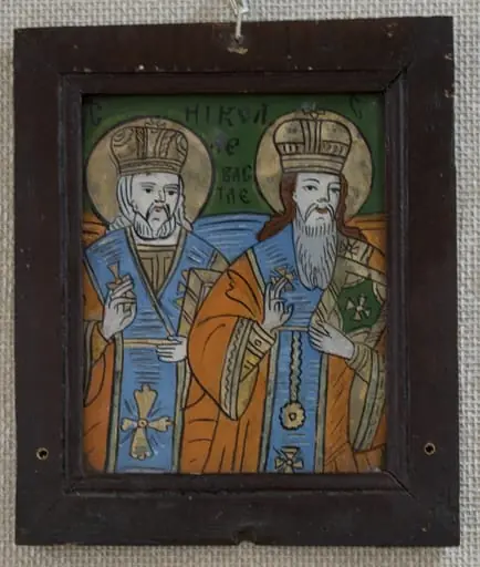 Icoana este pictată pe dosul unei bucăți de sticlă dreptunghiulară, în ax vertical; Sunt reprezentați sfinții ierarhi Nicolae al Mirelor Lichiei și Vasile cel Mare, într-o asociere mai puțin întâlnită. Cei doi sfinți sunt redați 3/4, din ușor semiprofil, privind către stânga lor. Cu dreapta binecuvintează cu degetul inelar unit cu cel mare, în stânga țin o carte sfântă la piept. Poziția este mai puțin uzitată: sfântul Nicolae este plasat puțin în spatele sf Vasile, creînd perspectivă. Ambii sunt înveșmântați cu sacosuri roșu cărămiziu cu borduri aurite, stihare orange cu mânecuțe, aurite, omofor bleu cu chenar și cruci aurite. Pe cap au mitre rotunde, înalte, bipartite. Sfântul Vasile are la gât un engolpion circular, confundat probabil cu o decorațiune. Sfântul Nicolae are barba scurtă, părul lung, alb, iar sfântul Nicolae are babrba lungă, albă și părul castaniu. Câmp verde întunecat, cu porțiuni de bleu și orange în dreptul umerilor sfinților, corespunzător culorilor veșmintelor. Inscripția este scrisă cu negru, cei doi S fiind plasați în colțuri,. Compoziția este ușor comprimată. Rama este alcătuită din patru șipci drepte, îmbinate oblic la colțuri, profilate pe o porțiune mică la interior, vopsite cu o culoare maron închis-roșcat, peste care s-a aplicat un lac lucios. Are trei găuri circulare, suscentral și lateral jos, pentru a fi prinsă oblic(mai târzii) Dosul este realizat din brad, fixate în cuie., by anonim