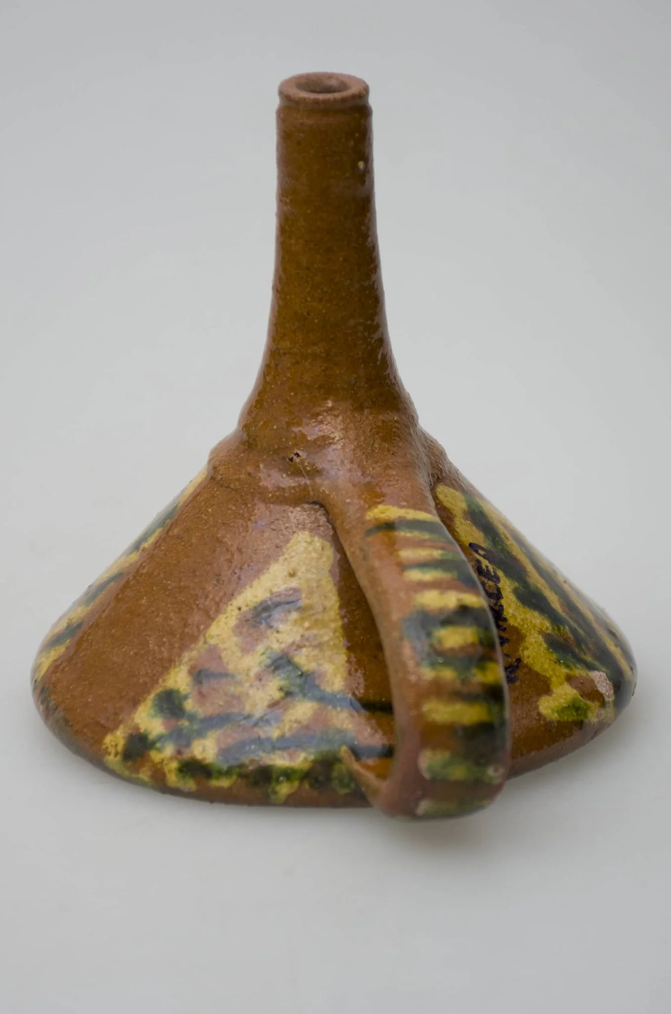 Pâlnie ceramică smălțuită, de formă tronconică, cu gura astupată cu o suprafață de lut găurită, formând o sită. La cealaltă latură a conului pâlnia este continuată printr-un tub cilindric, care se folosește la scurgerea lichidelor. Piesa de uz casnic este dotată cu un mâner care pleacă de la buză până la tubul cilindric de scurgere. Pe suprafața obiectului apar motive geometrice realizate cu pensula. Cromatică: fond: maro; motive: galben; verde., detail