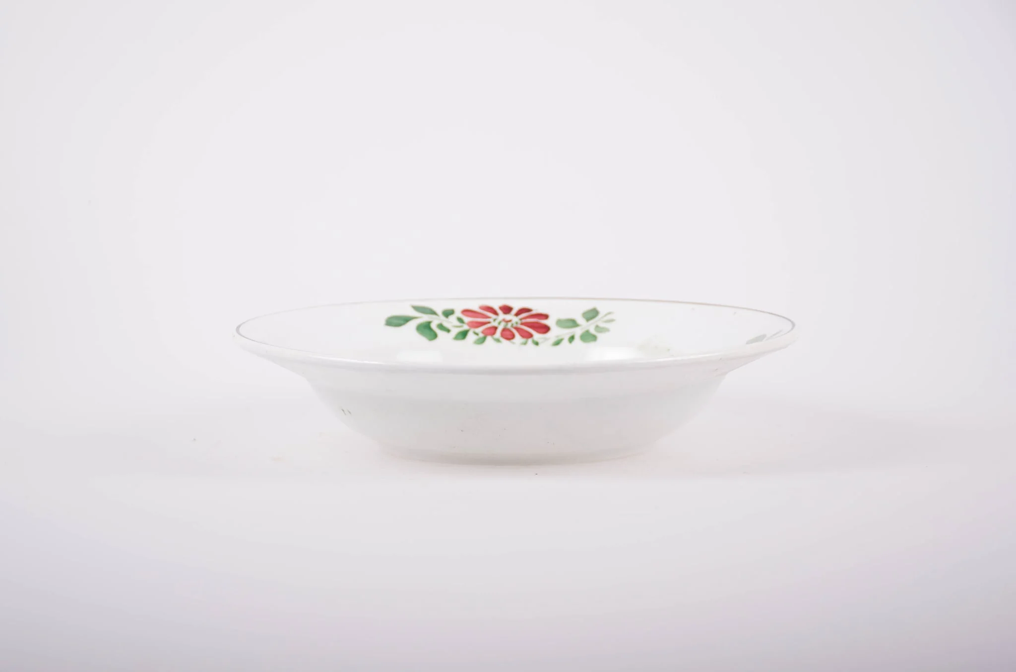 Farfurie de porțelan de formă tronconică, smălțuită în interior și la exterior. Pe fond alb avem flori stilizate (margarete). Buza farfuriei este conturată de o dungă neagră, iar pe margini sunt flori vișinii cu frunze verzi; în interiorul farfuriei pictate avem două flori mari (vișinii) și frunze verzi., detail