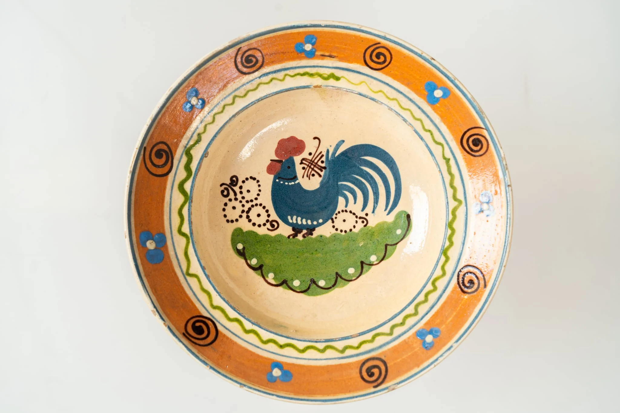 Formă adâncă, cu buză lată, răsfrântă. Piesa este modelată la roată, angobată cu humă albă. Decorul este realizat prin pictare cu pensula și cu cornul. Decorul, dispus pe întreaga suprafață a farfuriei, este format dintr-un motiv avimorf (cocoș, în zona centrală a farfuriei), motive florale și vegetale stilizate (central și pe buză) și motive geometrice (puncte, linii sub formă de cerc, linie vălurită, linie spiralată). Fața interioară a farfuriei este smălțuită cu un smalț transparent, lucios. Cromatica: alb, verde, albastru, brun, maro, siena naturală., detail