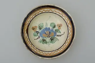 Blid de formă tronconică cu buza evazată. Smălțuit. Decorat cu motive florale: buchet, plasat pe fundul vasului și motive geoemtrice plasate pe gură: alternantă de cercuri și spirale ce se închid îm cerc. Cromatică: fond: alb; motive: maro; crem; verde; albastru.