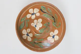 Blidul de formă tronconică adânc, smălțuit (la interior). Acesta este ornamentat cu motive florale, având cu buza înaltă. Blidul este neornamentat la exterior, fiind smălțuit (la exterior) doar pe buză. Pe exteriorul buzei este incizată o linie. Fundul obiectului are formă circulară, fiind prevăzut cu două orificii pentru prindere. Cromatică: fond: cărămiziu (exterior); alb (interior); decor: verde; alb; albastru; maro.