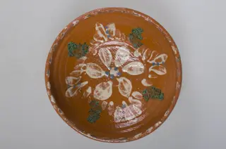 Blidul de formă tronconică este unul adânc, smălțuit pe interior, ornamentat cu motive florale, cu buză înaltă, neornamentat la exterior. Obiectul este smălțuit, la exterior, doar pe buză. Acesta prezintă puncte pictate cu pensula pe buză, la interior. Blidul este prevăzut cu două orificii pentru prindere, pe fund. Cromatică: fondul este cărămiziu, iar motivele sunt pictate cu alb, verde și albastru., 1850