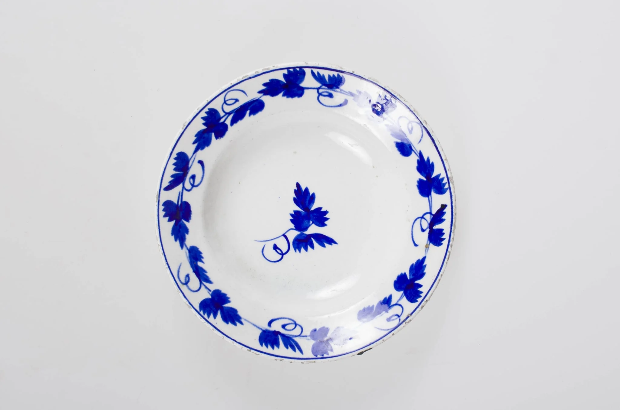 Obiect de uz casnic de formă tronconică. Pe fond alb se regăsește un ornament albastru: central două frunze de viță de vie. Pe margine farfuria este decorată cu frunze de viță de vie cu vrej și cu un cerc albastru. Cromatică: fond: alb; motive: albastru., detail