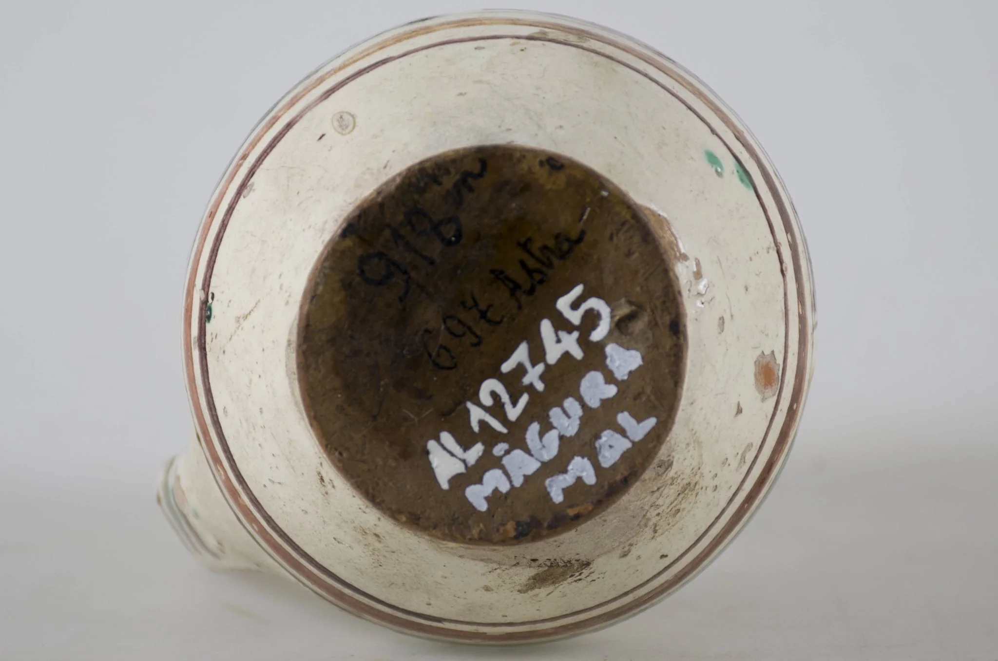 Vas ceramic smălțuit de mici dimensiuni, piriform, cu baza plată și bombat în zona „pântecelui”. Prezintă o toartă ce pornește din zona gâtului redus ca dimensiuni și se termină în zona diametrul maxim al vasului. Decorul vasului este compus din trei registre picturale. În primul registru au fost pictate două flori albe pe fundal verde și o a treia pe fundal maro, fiind despărțite prin linii de culoare galbenă. Cel de-al doilea registru a fost decorat cu motive geometrice stilizate, linii și triunghiuri afrontate de culoare galbenă, pe fundal de culoare verde. Ultimul registru a fost decorat cu linii de culoare maro și galben, asemenea cu trei brazi și înconjurate de câte două frunze de culoare verde. Toate cele trei registre picturale sunt încadrate de câte trei linii concentrice (două subțiri și una lată) de culoare maro-închis și maro-roșcat. Pe toartă este decorat cu linii paralele orizontale. Cromatică: fond alb; motive: galben; verde; maro., detail