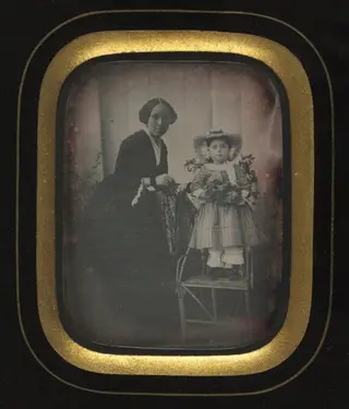 Child Standing on a Chair Holding Flowers, with Mother