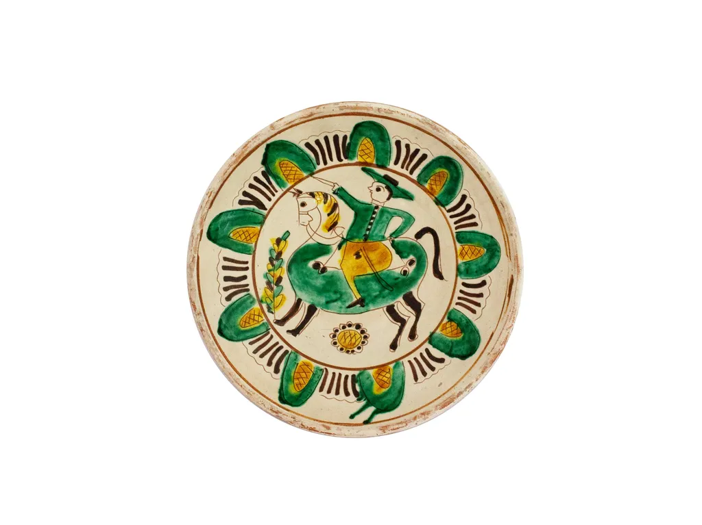 Strachină lucrată în manieră Kuty, de formă tronconică, modelată la roată; decor geometrizat și naturalist amplasat pe toată suprafața vasului organizat în două registre despărțite de linii circulare realizate cu cornul: central prezintă un motiv antropomorf: călăreț cu sabia în mână încălecat pe cal și motive fitomorfe: floarea soarelui și brăduț; spre marginea vasului un registru cu motive geometrice semiovoidale realizate cu linii curbe și hașuri, despărțite de grupuri de liniuțe; cromatică: fond alb dat de angobă, decor realizat cu verde, galben, brun și cărămiziu. Pe exterior este imprimată ștampila cu numele meșterului scris cu majusculă și caractere italice: Colibaba., by Colibaba Constntin, 1973