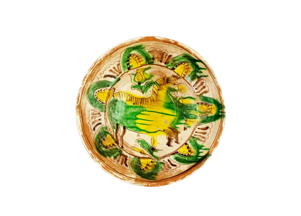 Strachină lucrată în manieră Kuty, de formă tronconică, modelată la roată; decor geometrizat și naturalist amplasat pe toată suprafața vasului organizat în două registre despărțite de linii circulare realizate cu cornul: central prezintă un motiv zoomorf: animal, înconjurat de motive fitomorfe: flori de lalea și frunze; spre marginea vasului un registru cu motive geometrice semiovoidale realizate cu linii curbe și puncte, despărțite de grupuri de liniuțe; cromatică: fond alb dat de angobă, decor realizat cu verde, galben și brun. Pe exterior este imprimată ștampila cu numele meșterului scris cu majusculă și caractere italice: Colibaba., by Colibaba Constntin, 1974