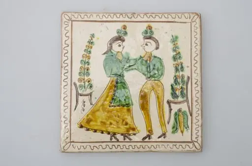 Piesă ceramică de formă pătrată, smălțuită și angobată, cu rol decorativ. Laturile pătratului sunt marcate de două chenare, primul vălurit, al doilea în linie dreaptă. Ornamentată cu motive antropomorfe și floral-vegetale: doi tineri, un băiat și o fată ținându-se pe după mijloc (băiatul cu mâna dreaptă, fata cu stânga). În spatele lor câte un scaun din care se înalță o floare. Motivele au fost la început incizate, iar apoi pictate. Pe spate, cahla este prevăzută cu un orificiu pentru prinderea aței. Tot aici, este inscripționat numele meșterului olar, "Colibaba". Cromatică: fundal alb; motive: verde, galben, cărămiziu, maro, negru., by Colibaba Marcel