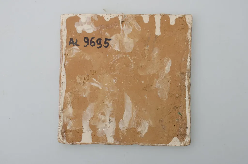 Piesă ceramică de formă pătrată, smălțuită și angobată, laturile pătratului fiind marcate de două chenare, primul vălurit, al doilea în linie dreaptă. Ornamentată cu motive zoomorfe și floral-vegetale, după fabula lui La Fontaine, Vulpea și barza: o vulpe care bea dintr-un ulcior și o barză care mânâncă dintr-un vas plat aflat pe o măsuță joasă. Pe două din colțuri, două flori completează pictura. Motivele au fost la început incizate, iar apoi pictate. Pe spate, cahla este prevăzută cu un orificiu pentru prinderea aței. Tot aici, este inscripționat numele meșterului olar, "Colibaba". Cromatică: fundal alb; motive: verde, galben, maro, cărămiziu., by Colibaba Marcel, unspecified