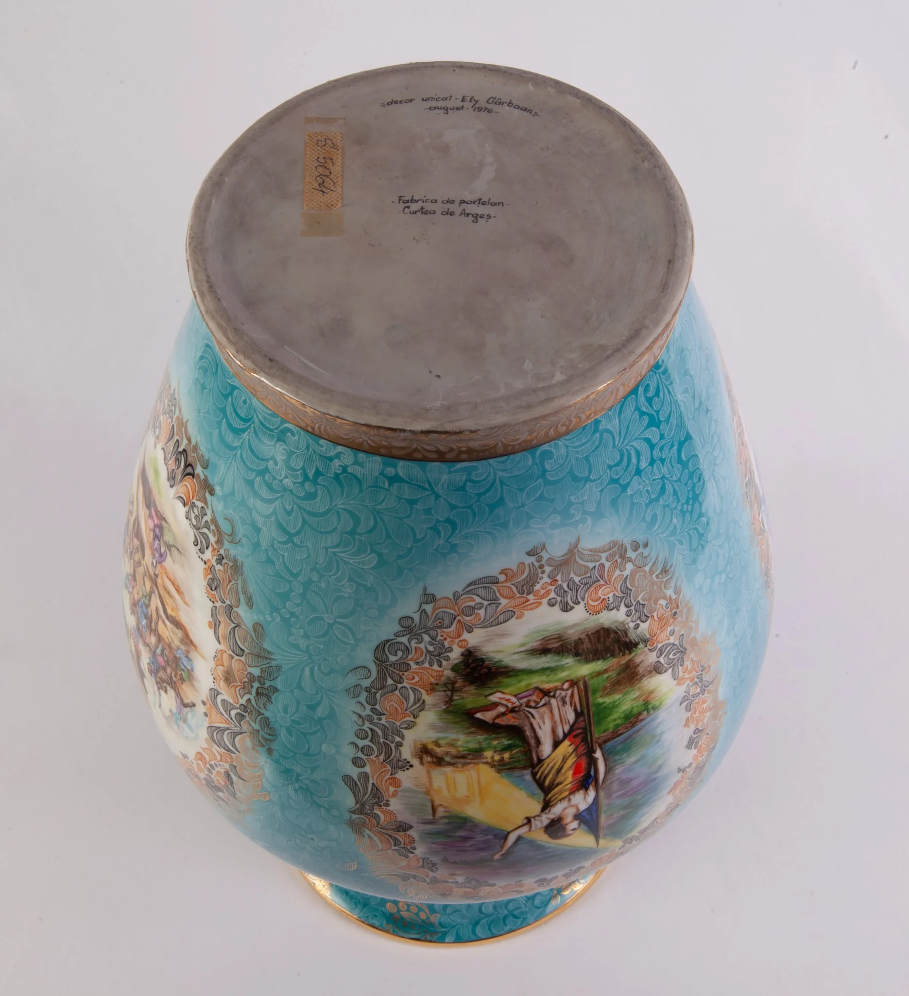 Vas mare din porțelan bleu cu auriu, decorată cu patru medalioane încadrate cu motive florale. Primul medalion reprezentarea unei bătălii din perioada medievală; al doilea medalion reproducerea lucrării lui C. Rosenthal ”România rupându-și cătușele pe Câmpia Libertății”; cel de-al treilea medalion prezintă o scenă de luptă din perioada Marelui Război. Cel de-al partulea medalion prezintă stema RSR, steagul tricolor și un citat dintr-un discurs a lui Nicolae Ceaușescu ”....actul de la 23 August nu a venit din cer ci a fost rezultatul luptelor îndelungate ale poporului român”. Buza vazei este decorată cu o bandă metalică aurie. Pe verso numele artistului Ely Gârboan. Vază oferită lui Nicolae Ceaușescu de reprezentanții Fabricii de Porțelan Curtea de Argeș cu ocazia vizitei de lucru din jud.Argeș, 17 septembrie 1976., detail