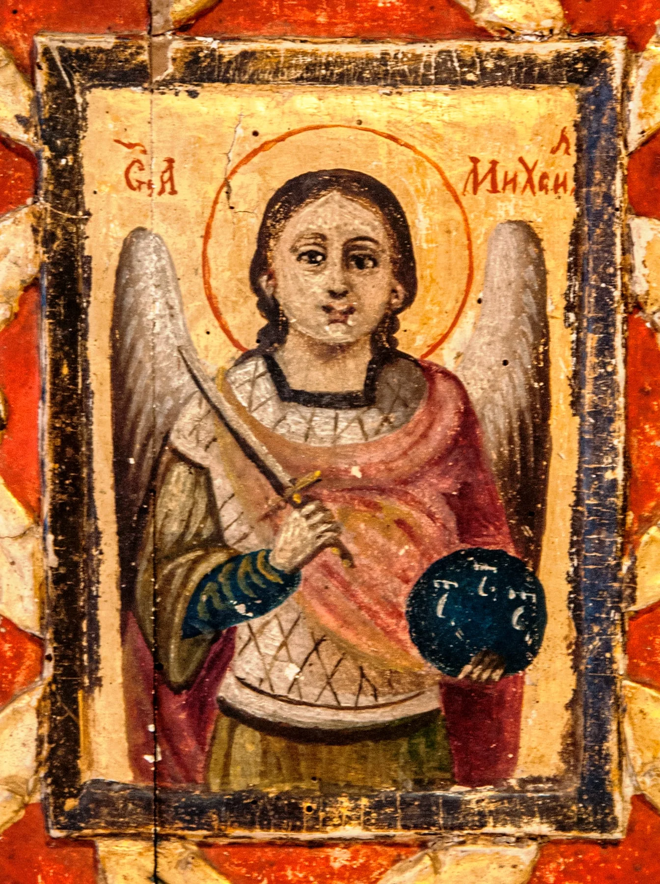 Într-un spațiu central dreptunghiular în relief este pictat Arhanghelul Mihail 3/4. Arhanghelul ține în mâna dreaptă sabia ridicată, în stânga globul pământesc cu însemnele dumnezeirii. Este redat tânăr, cu fața rotundă, expresivă, părul lung, lăsat pe umeri.Poartă o tunică verde, cămașă albastră și lorică argintie, peste care este prinsă mantia lungă, roșie.Aripile sint strânse, aureola conturată cu o linie roșie fină, se proiectează pe fondul auriu unde este scrisă în partea superioară inscripția, cu litere de culoare roșie.Chenar îngust, negru. Decorul ancadramentului, sculptat, în relief : 8 flori cu patru petale rotunde, pictate cu albastru, centrul cu roșu, iar frunzele aurii. Spațiul dintre flori. La nivelul suportului, pictat cu roșu. Suportul este crăpat, cele două bucăți care îl alcătuiesc nu se mai sudează. După modul de realizare se pare că icoana a aparținut unei biserici., detail