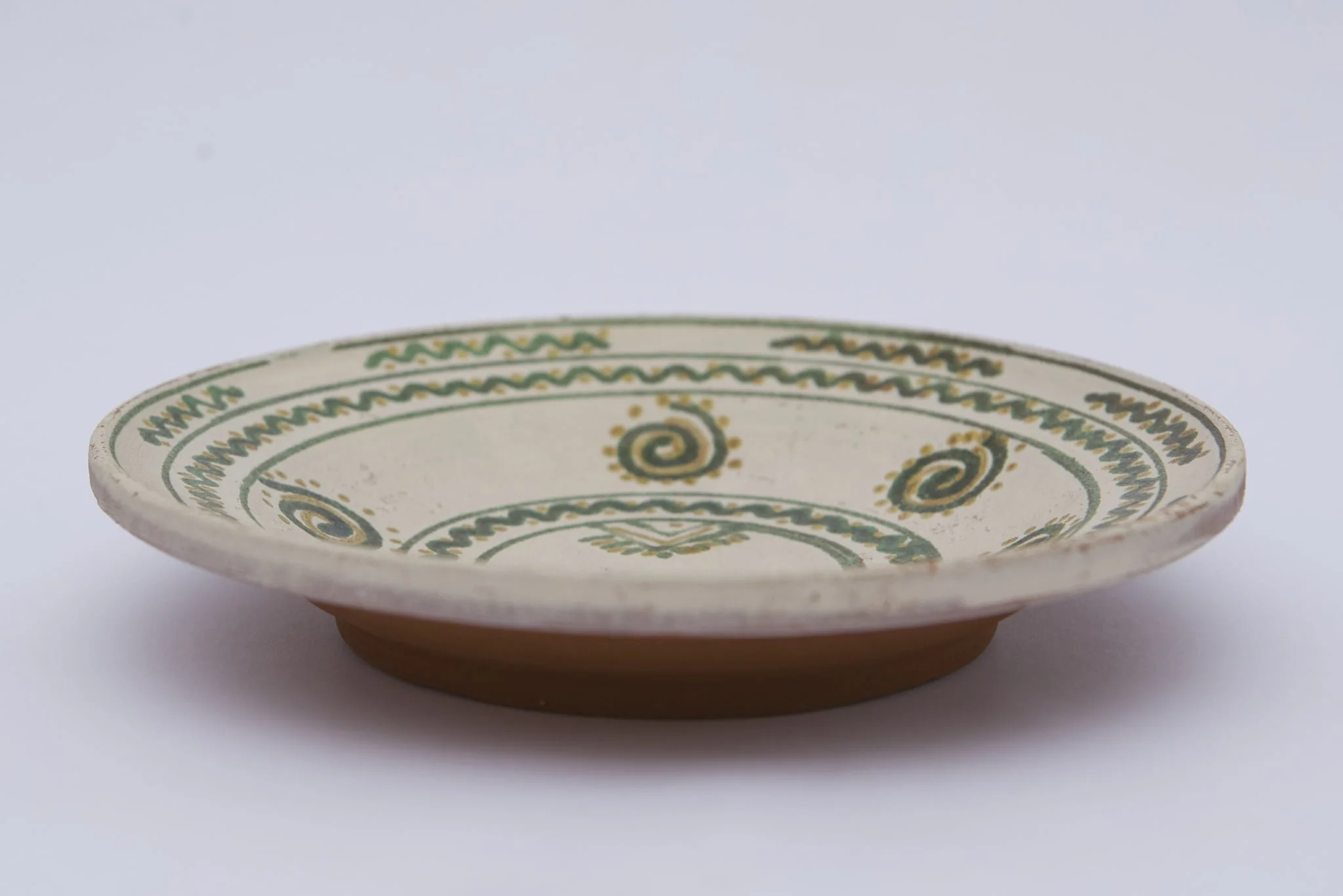 Vas ceramic de formă discoidală pe bază puțin înălțată. Fața farfuriei a fost introdusă în angobă albă, decorația a fost făcută cu pensula. Pe fundul vasului sunt două cercuri concentrice: în primul sunt doi brăduți, iar în al doilea valul punctat. Pe pereți sunt șase spirale punctate. Marginea vasului a fost împărțită în două registre, primul cu val punctat, în al doilea sunt șapte valuri întrerupte. La posterior, pe fund, semătura ”D Șchiopu ''. Pentru atârnare baza este perforată. Cromatică: fond: alb; motive; verde; galben., detail