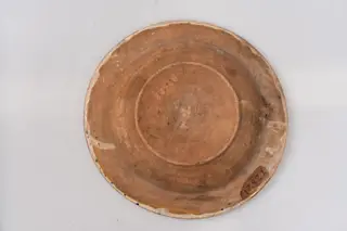Farfurie adâncă cu buză evazată; este acoperită pe suprafața interioară cu un strat de angobă albă peste care este pictat cu cornul și cu pensula decorul monocromatic format din motive florale și vegetale stilizate: registrul central de pe fundul farfuriei conține un buchet format dintr-o floare de crin și două flori rotunde cu petale formate din linii drepte și patru grupuri de puncte sugerând niște flori mici. De o parte și de alta a florii de crin apare înscris anul fabricării piesei, 1794. Registrul decorativ de pe buza farfuriei, încadrat între două linii circulare, se compune dintr-un șir continuu format din opt flori mici de lalea cu tije în formă de S și frunze, sugerate prin linii paralele și puncte. Muchia buzei este decorată cu mici linii paralele. Suprafața ornamentată a farfuriei este acoperită cu un strat de smalț transparent. Cromatica: alb, albastru.