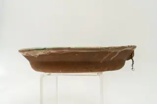 Farfurie adâncă, cu buza răsfrântă, modelată la roata olarului, angobată cu humă albă pe fața interioară. Decorul, bogat, este realizat prin pictare cu pensula și cu cornul și se compune din motive decorative florale stilizate și geometrice, acoperind întreaga suprafață a farfuriei. Cromatica: alb, verde, galben ocru, maro., 1850