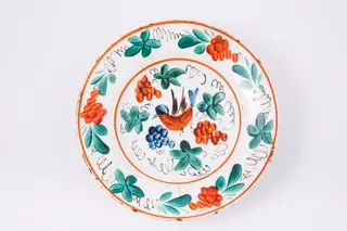 Farfurie adâncă, cu marginea lată și evazată, ușor îndoită spre interior. Marginea este decorată cu trei grupuri de buchete alcătuite dintr-o floare roșie și frunze, intercalate de trei motive fitomorfe și ramuri stilizate. Decorul central reprezintă o pasăre în cromatică roșu și albastru, cu aripi maro, înconjurată de trei buchete, două compuse din flori roșii și unul din flori albastre, intercalate de patru frunze și ramuri stilizate. Piesa prezintă pe spate o ștampilă, indescifrabilă. Cromatică: alb, roșu, verde, albastru, maro.
