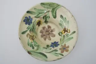 Farfurie cu marginea foarte lată și evazată, smălțuită în interior. Decor floral pe toată suprafața interioară. Cromatică: fond: alb; motive: brun; verde; galben; albastru., 1850