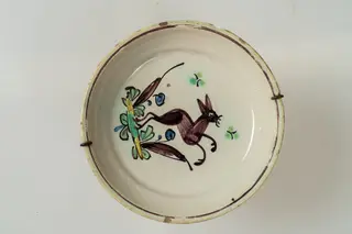 Farfurie de formă semi-adâncă, cu baza largă și cu buza lată, răsfrântă, cu muchia buzei ușor concavă spre exterior. Decorul, dispus pe un fond alb, prin pictare, este format dintr-un motiv zoomorf (căprioară) și vegetal stilizat, plasat central, pe fundul farfuriei. Muchia buzei este marcată de o linie sub formă de cerc. Cromatica decorului: alb, verde, brun, galben, albastru., 1850