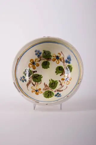 Farfurie de formă tronconică, adâncită, cu buza foarte înaltă; pe fund are găuri pentru agățare. Este smălțuit în interior și exterior (buza). Decorat cu motive geometrice: linie; motive fitomorfe; motive florale. Cromatică: fond: alb; motive: verde; maro; albastru., 1850