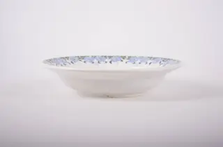 Farfurie de formă tronconică, adâncită; pe fund are găuri pentru agățare. Pe toată marginea este decorată cu motive florale, iar pe fund are trei cercuri concentrice. Cromatică: fond: alb; motive: albastru; verde., 1850