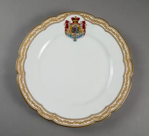 Farfurie de porțelan de Sevres, realizată din porțelan alb, cu margini treflate, decorate cu frunze de laur pictate, în centrul decorațiilor având blazonul familiei Suțu. Blazonul a fost adesea confundat cu cel al Principatelor Unite, fiind format din: stemele celor două țări românești: prima cea a Moldovei, cea de-a doua cea a Țării Românești, steme plasate pe două scuturi ovale, în fascie, acolate, puțin suprapuse, cea a Moldovei având capul de bour de argint cu stea în șase colțuri de aur, pe un scut cu segmente verticale egale roșii și albastre; cea a Țării Românești având acvila cruciată de argint, cu crucea de aur, scutul având segmente verticale galbene și albastre. Cele două scuturi au ca tenanți doi lei aurii, deasupra armele familiei Suțu – iataganul și sabia, ambele aurii, precum, pe un pavilion de purpură căptușit cu hermină, brodat cu ciucuri de aur și prins într-o coroană cu pietre scumpe. Pe scut, în partea inferioară se află și decorațiile familiei Suțu. Familia Suțu a fost o familie fanariotă grecească, venită în principate în cea de-a doua parte a secolului al XVIII-lea, având trei domni în ambele țări Românești (Alexandru Suțu, Mihai Suțu și Grigore Suțu). Blazonul familiei poate fi admirat inclusiv pe clădirea Palatului Suțu, astăzi Muzeul de Istorie a Municipiului București. Farfuria are marca atelierului Sevres și modelul din anul 1844, precum și seria.