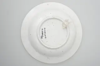Farfurie din porțelan, de formă tronconică, întrebuințată în gospodărie la decorarea pereților casei. În interior se identifică un decor fitomorf, motive florale și vegetale, precum și un decor geometric. Motive florare sunt dispuse în trei registre pe margine, încadrate de un cerc negru; în centru este decorat cu trei flori albastre cu frunze verzi. Cromatică: fond: alb; motive: albastru, negru, verde.