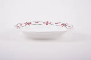 Farfurie din porțelan de formă tronconică. Pe fond alb, marginea este decorată cu flori stilizate. Cromatică: roșu și verde; interiorul farfuriei prezintă flori în: roșu; albastru; verde., 1950