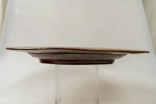 Farfurie foarte mare, de formă aplatizată, buză mare, răsfrântă. Piesa este modelată la roata olarului și decorată cu cornul și cu pensula, cu humă albă și pigment maro, pe fondul neangobat al piesei. Motivele decorative sunt florale și vegetale stilizate (dispuse central, pe fundul farfuriei și înlănțuite pe buza acesteia) și geometrice (linii sub formă de cerc, linie ondulată, puncte, zig-zaguri). Piesa este acoperită pe ambele fețe cu un smalț transparent. Cromatica: alb, maro., 1850