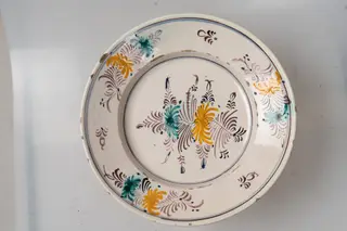 Farfurie mare, de formă aplatizată, cu buza răsfrântă. Decorul, dispus pe un fond alb-lăptos, fin realizat prin pictare cu pensula, este format din motive florale și vegetale stilizate, dispuse într-un registru central, pe fundul farfuriei (format din două flori, una galbenă și cealaltă verde-turcoaz, cu petale alungite, împreună cu frunze și elemente vegetale de culoare maro-brun, cu accente albastre) și pe buza farfuriei, unde regăsim trei grupuri de motive formate din același tip de flori ca cele din registrul central, dar de dimensiuni mai mici, grupuri separate de câte un mic motiv vegetal de culoare maro. Cromatica: alb, verde-turcoaz, maro-brun, albastru, galben-ocru.