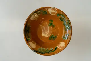 Farfurie mică, adâncă, de formă tronconică, cu buză lată, răsfrântă. Piesa este modelată la roata olarului, nefiind angobată. Decorul este realizat prin pictare cu pensula și constă în motive decorative florale și vegetale (flori și frunze), dispuse central, pe fundul farfuriei și pe toată buza acesteia, sub formă de ghirlandă. Cromatica: alb, verde. Farfuria este smălțuită pe interior, cu smalț transparent.