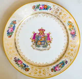 Farfurie, model decorativ stil Louis-Philippe, ales pentru serviciul de masa de peste 100 de piese Cuza, comandat la manufacturile regale din Sevres. Acesta urma să fie folosit de familia domnitoare Cuza în palatul de la Cotroceni. Farfuria este întinsă, circulară, pictată pe margini cu cinci medalioane florale care alternează cu arabescuri aurii. Este decorată central cu stema Principatelor Române și deviza unionistă „Toți în Unu". Stema și motivele florale se caracterizează printr-o vie policromie: galben, auriu, nuanțe de roșu, roz, verde și albastru. Pe reversul ei apar două marci în câmp circular: „Chateaux de Trianon" (culoare roșu carmin) și „Sevres 1846" (cu albastru). De asemenea, se remarcă cartelul care conține, în cifre latine, datele dublei alegeri a lui Al. I. Cuza ca principe al Moldovei și Țării Românești.